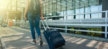 woman walking on pathway while strolling luggage